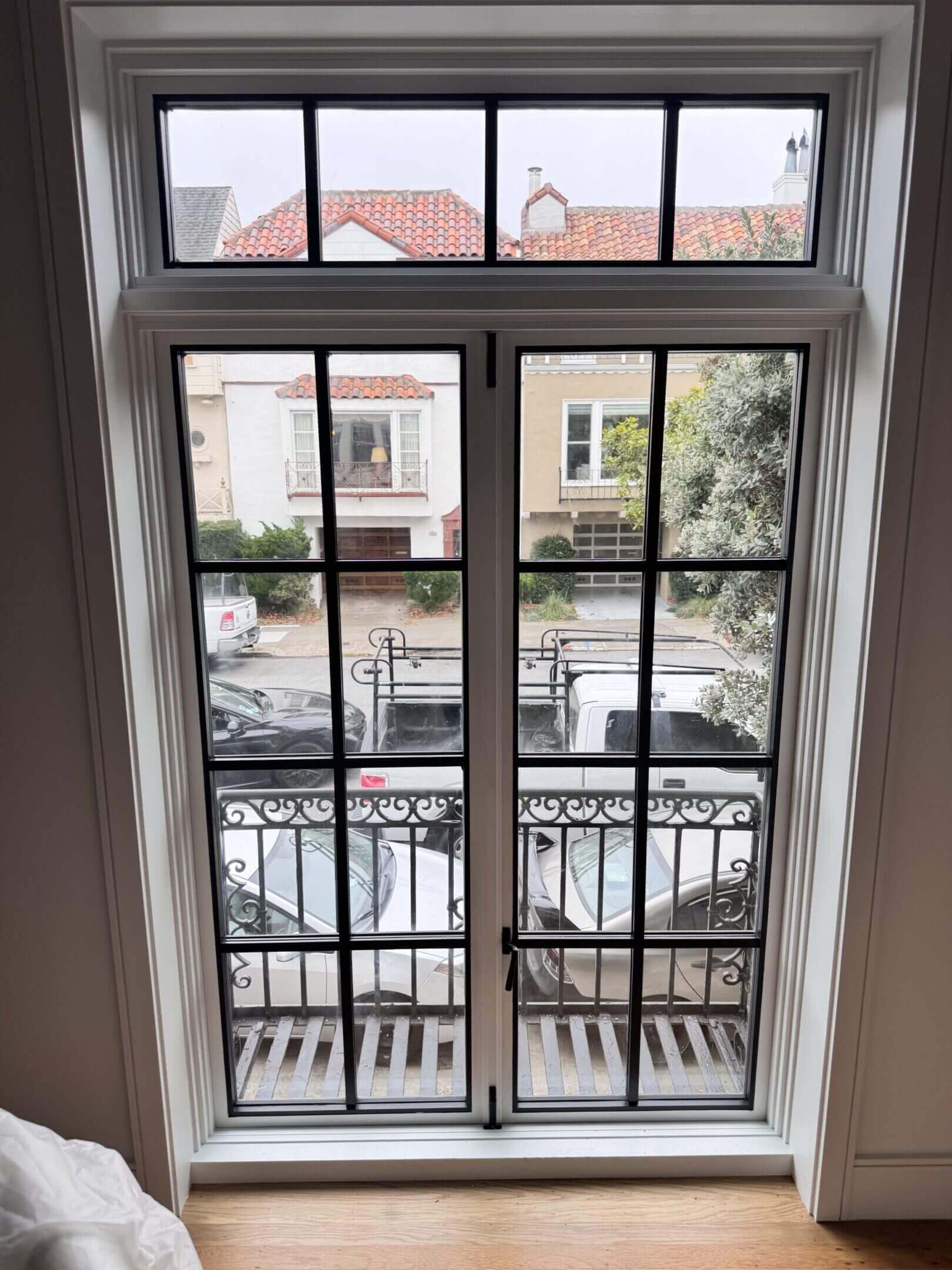 View through a window with balcony railing overlooking houses and parked cars.