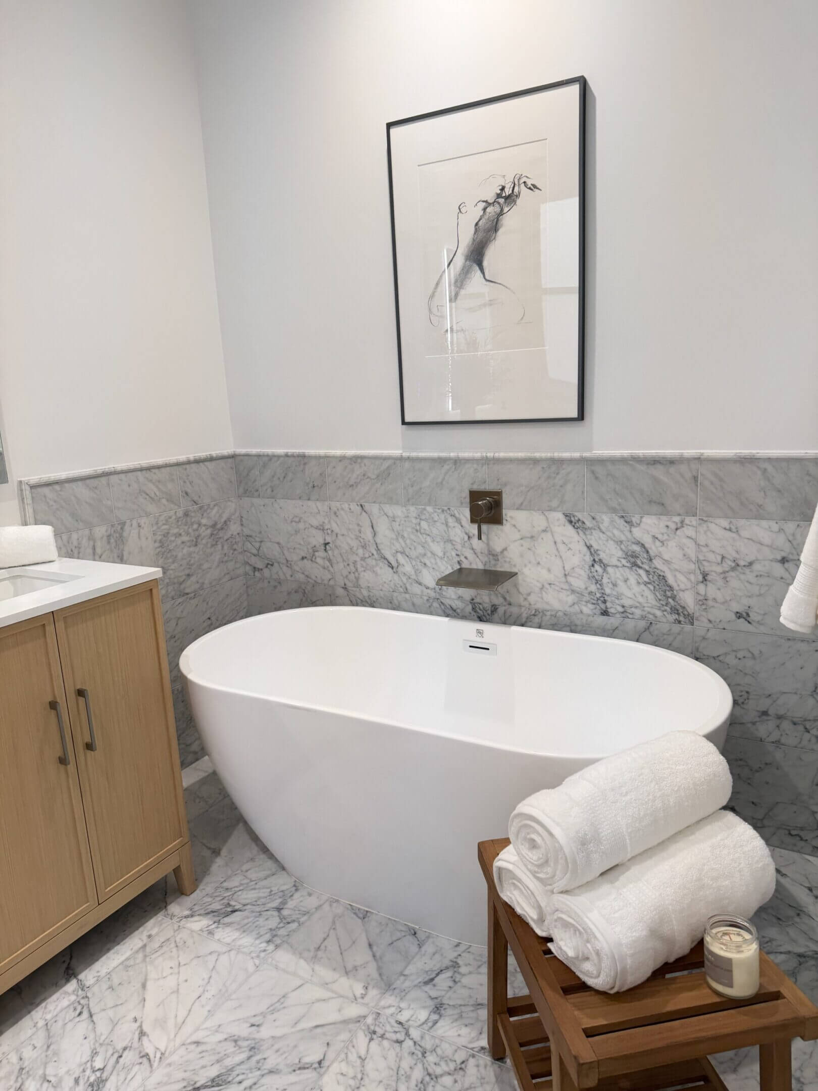 Modern bathroom with freestanding tub, marble backsplash, and wooden vanity.